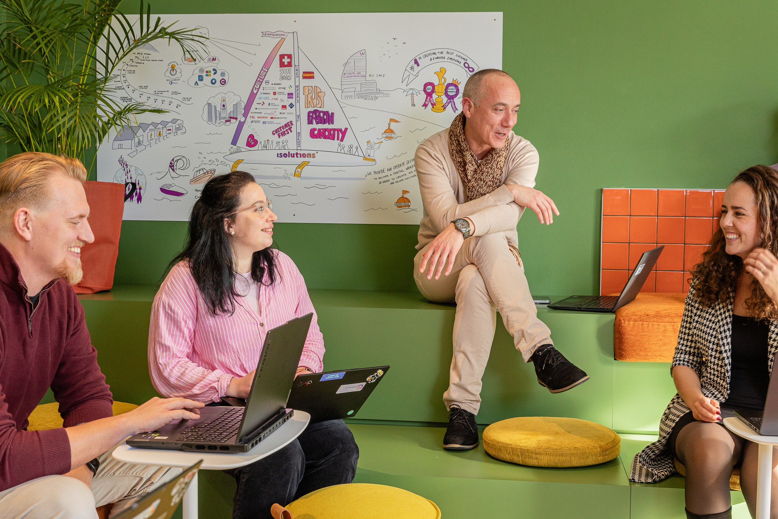 Team collaborating with laptops in informal meeting area with wall illustration