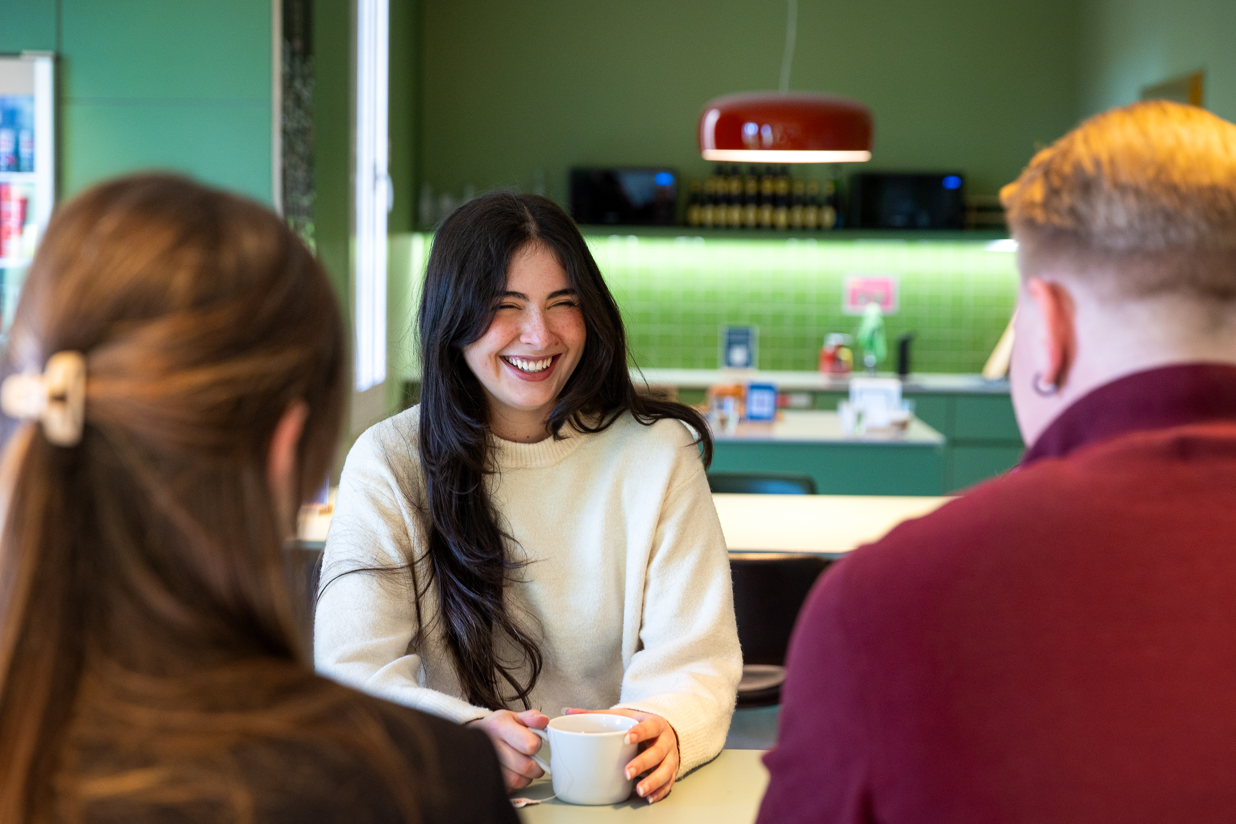 Person smiling while holding coffee during informal chat in office kitchen