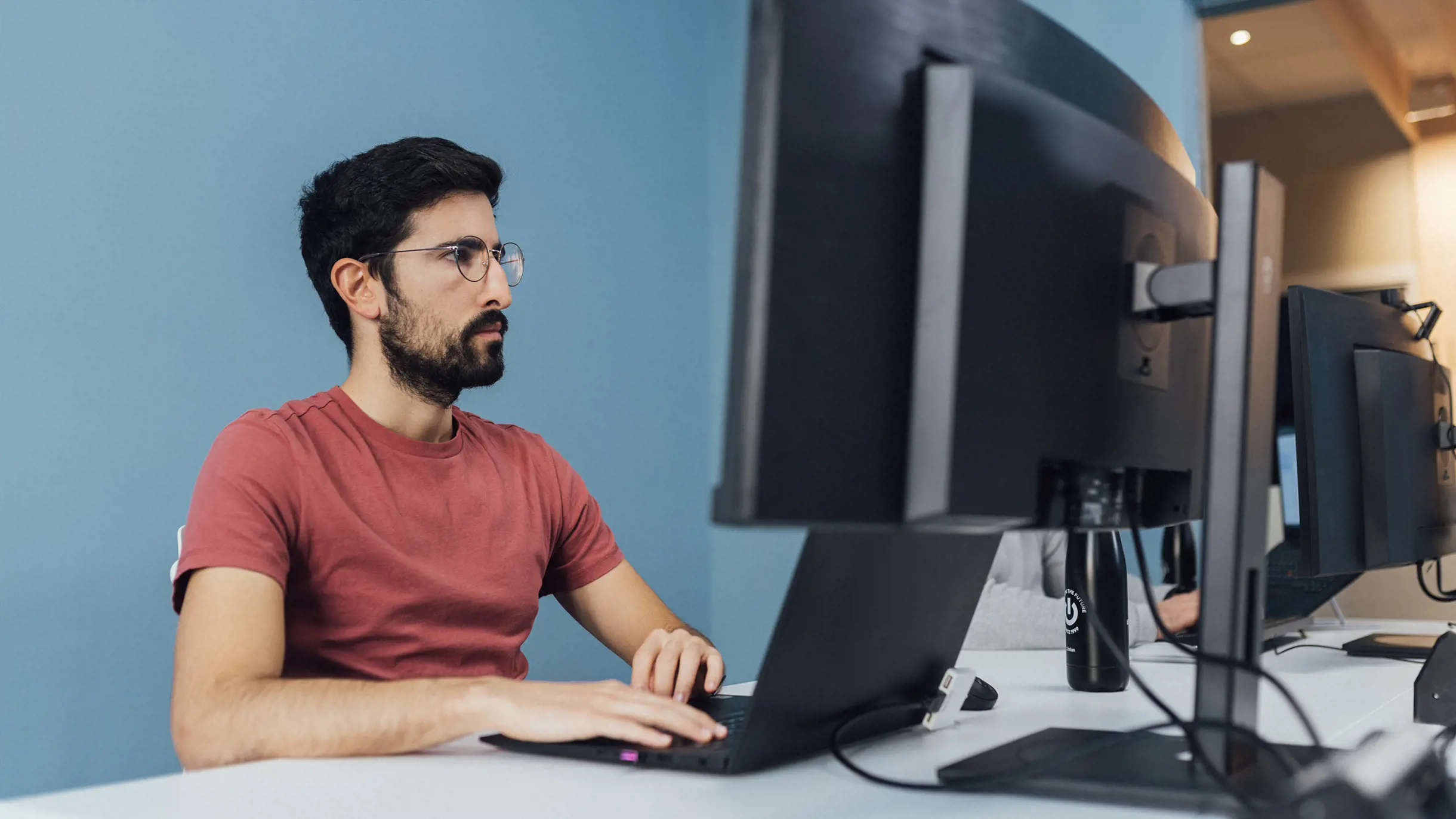 Man in red t-shirt concentrated on working with two screens
