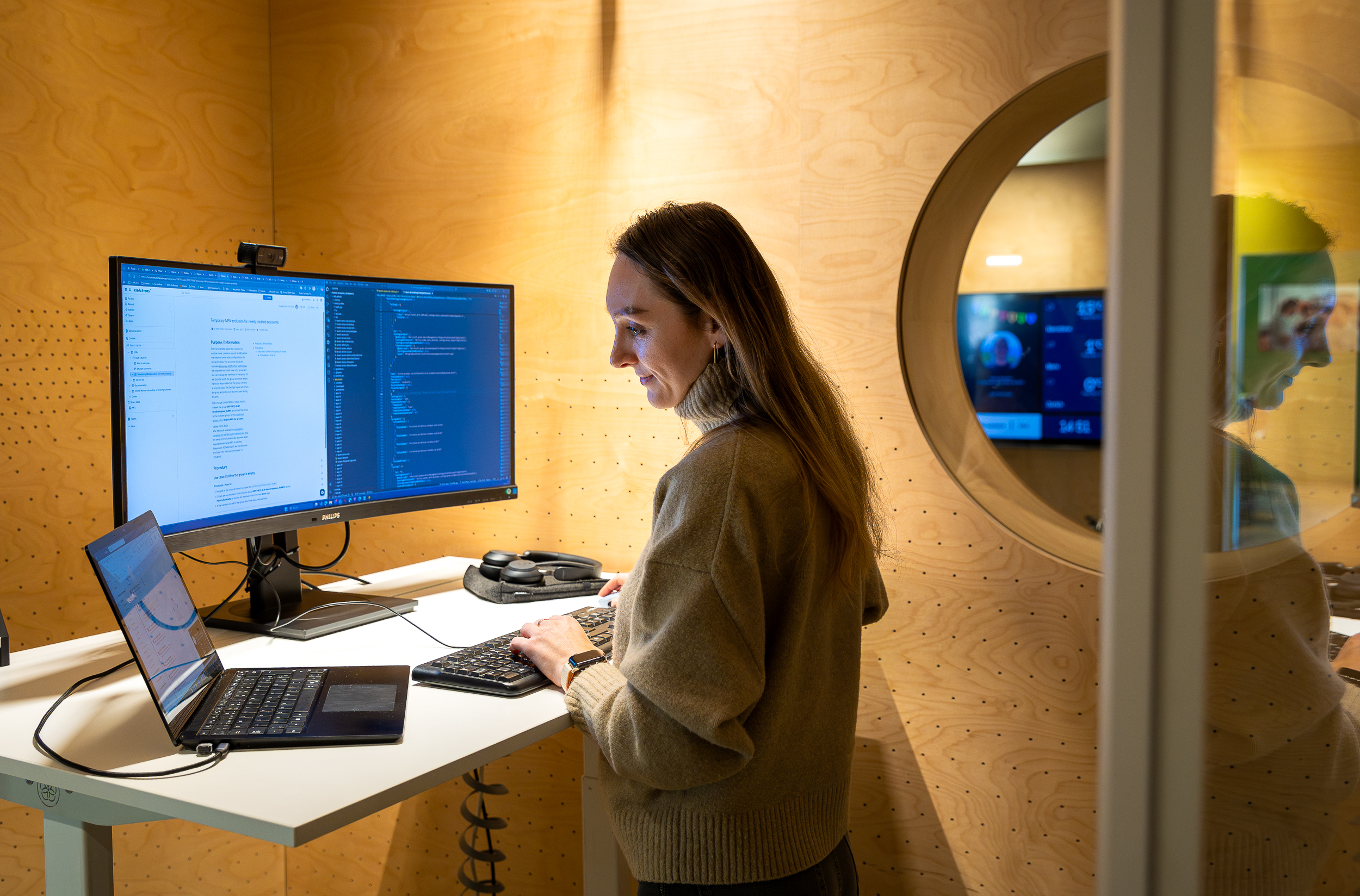 Person working at standing desk with dual monitors and laptop