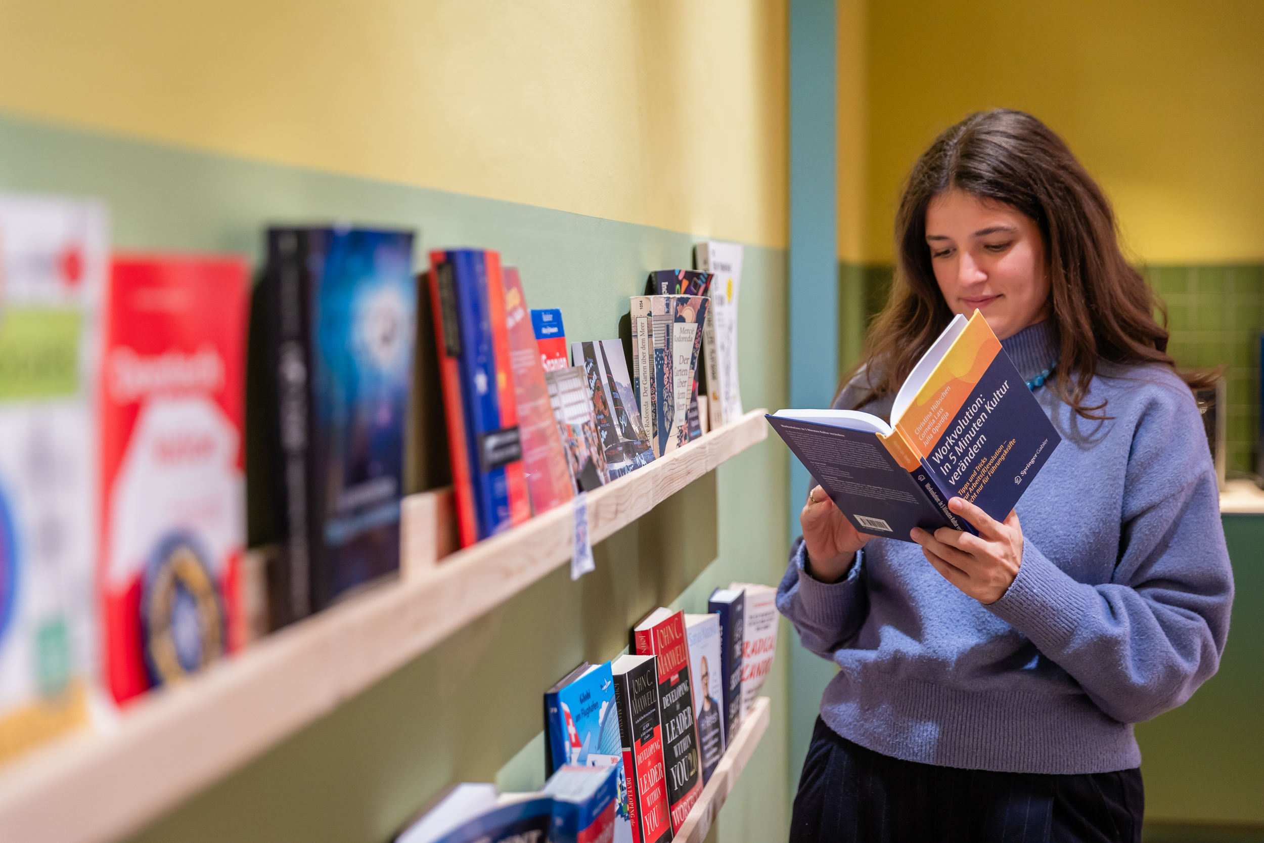 Person reading a book next to a modern office bookshelf with colorful books
