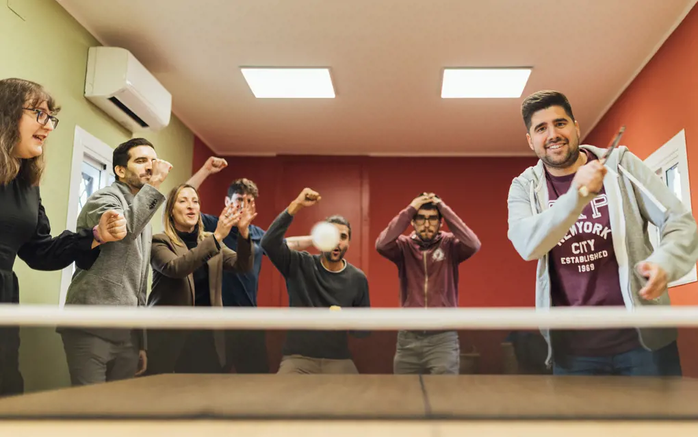 Group of People standing around a ping pong table cheering