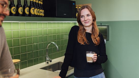 Woman having a coffee in a green kitchen while listening to her colleague