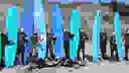 isolutions History Silicon Valley Sufer stehen nebeneinander und halten alle ein blaues Surfboard