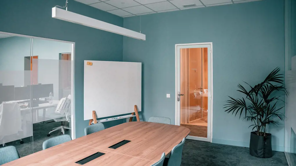 Meeting room with wooden table, blue chairs and a whiteboard in the back