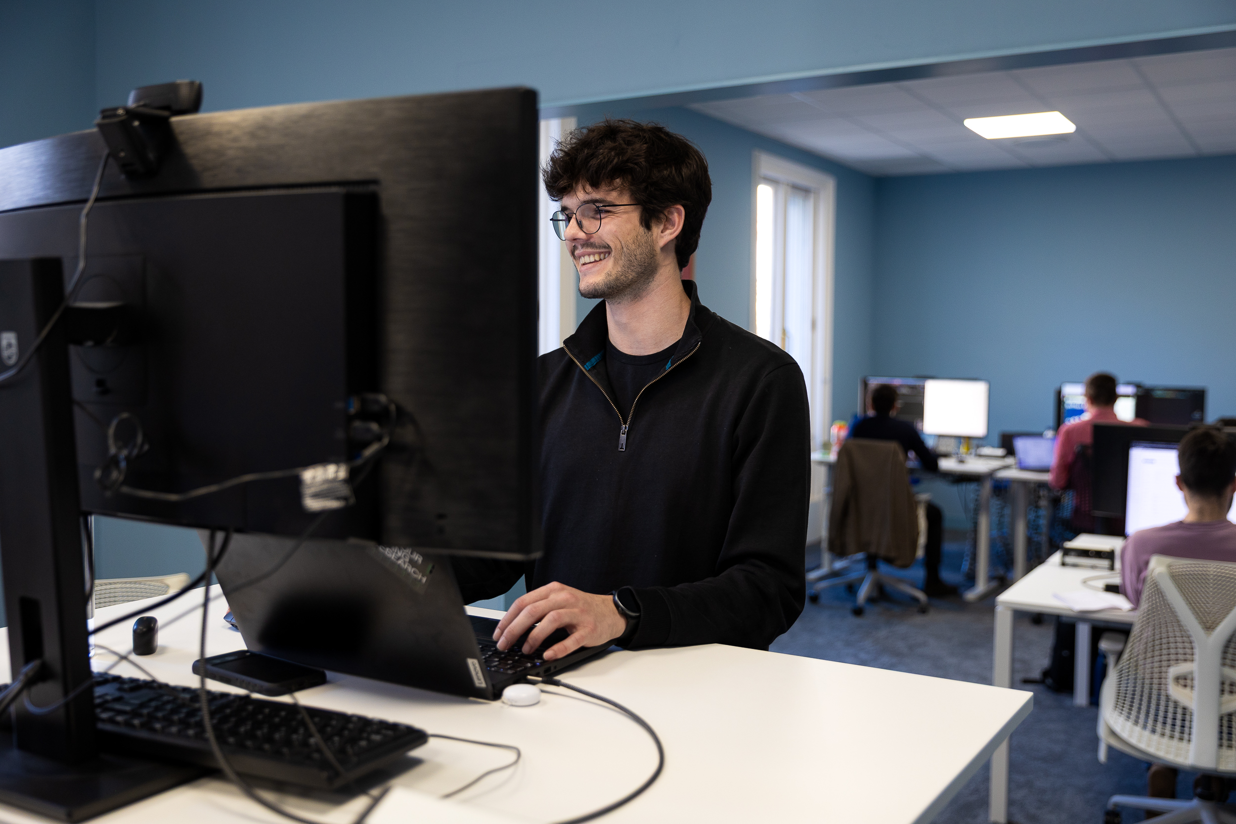 Men working at standing desk, looking at a screen smiling.