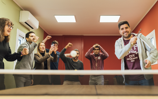 Group of people standing around a ping pong table cheering